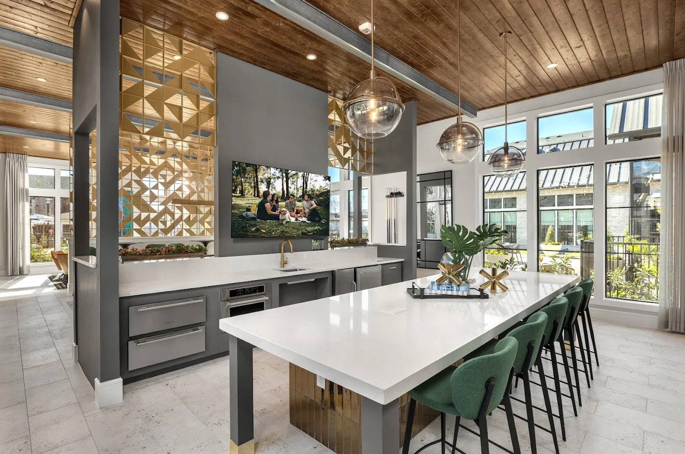 Clubhouse kitchen and bar with a wood ceiling, gold geometric screen, white island and green stools, Alexan Lake Olympia