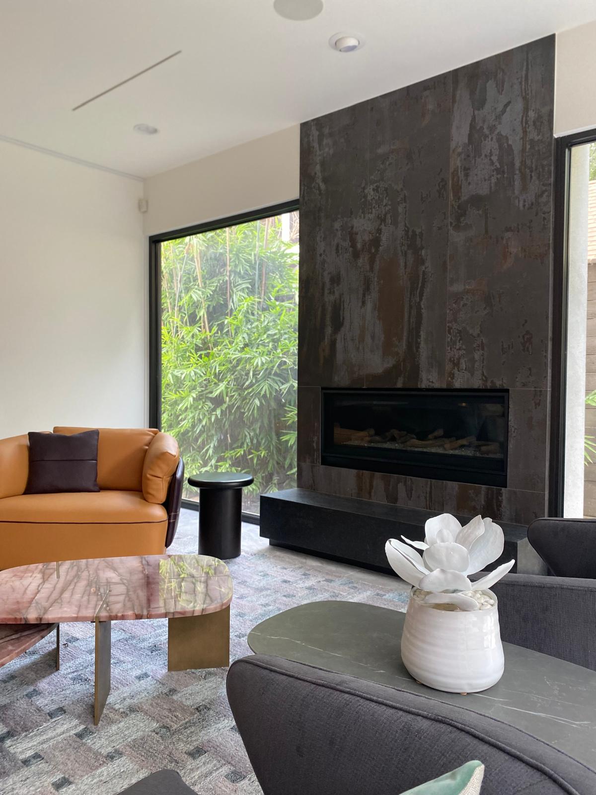Living room with a rusted metal fireplace wall, cognac leather chair and pink marble coffee table, Montrose